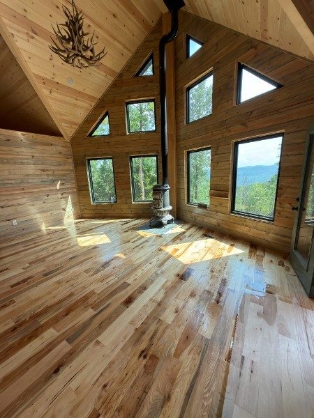Rustic hickory floor with a high-gloss finish in a wood-walled mountain cabin with tall windows and a wood stove