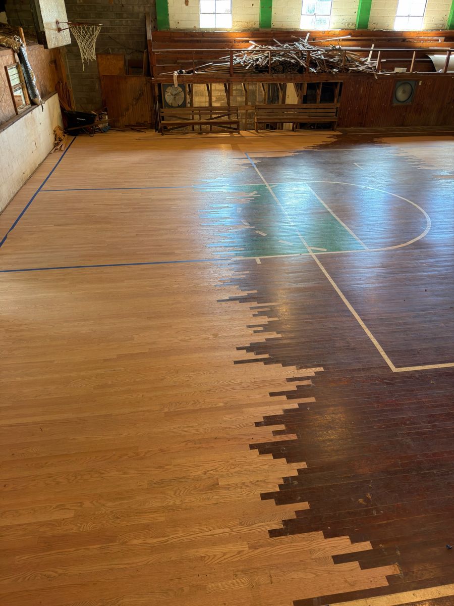 Old gymnasium court with new boards woven in board by board alongside the original dark-finished floor