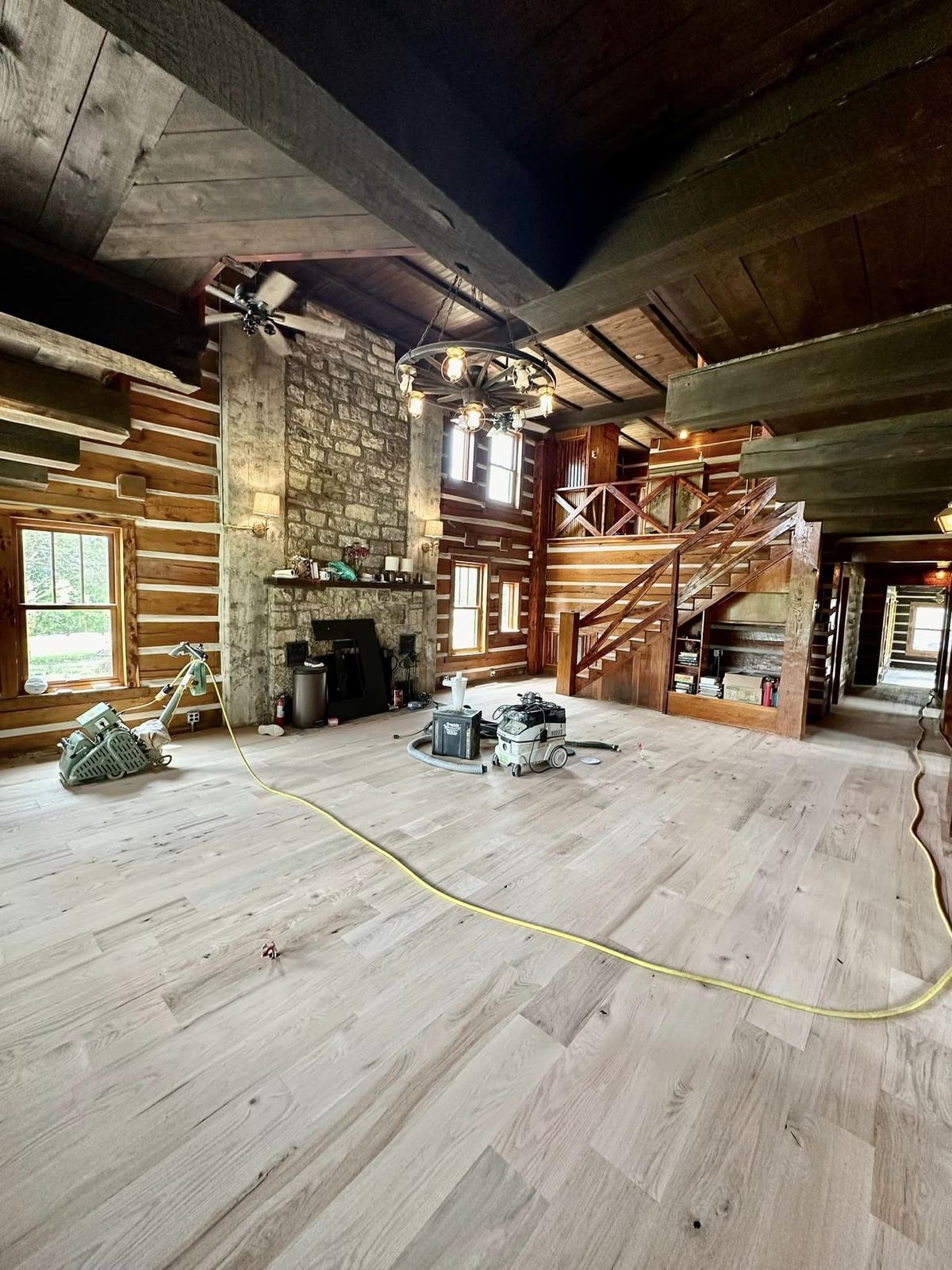 New light wide-plank floor in a 1940s log cabin with a stone fireplace and loft stairs